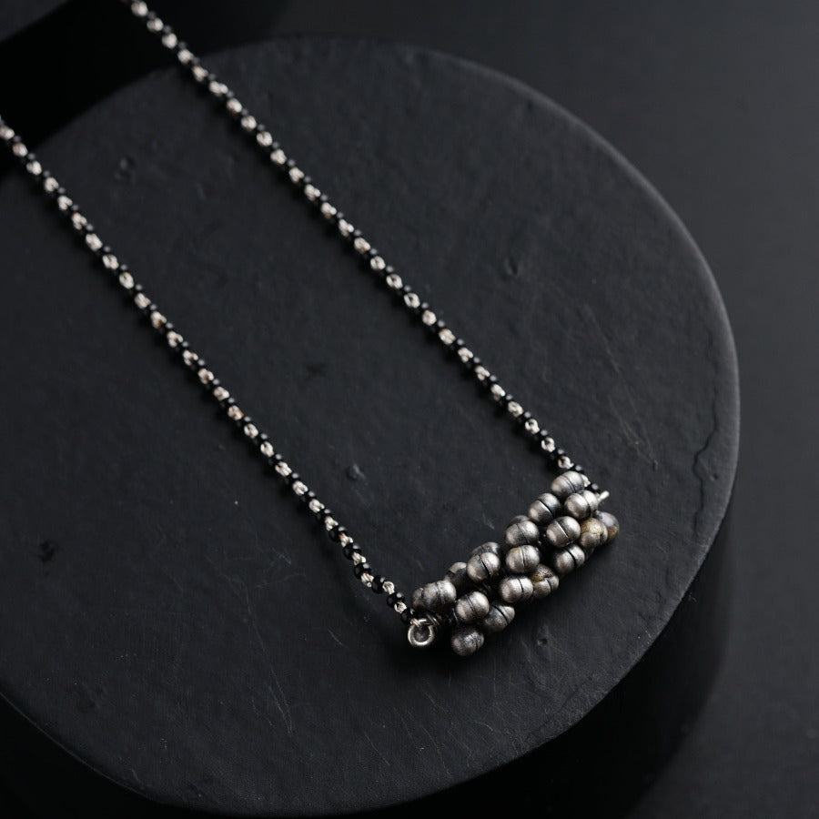 a silver beaded necklace sitting on top of a black surface