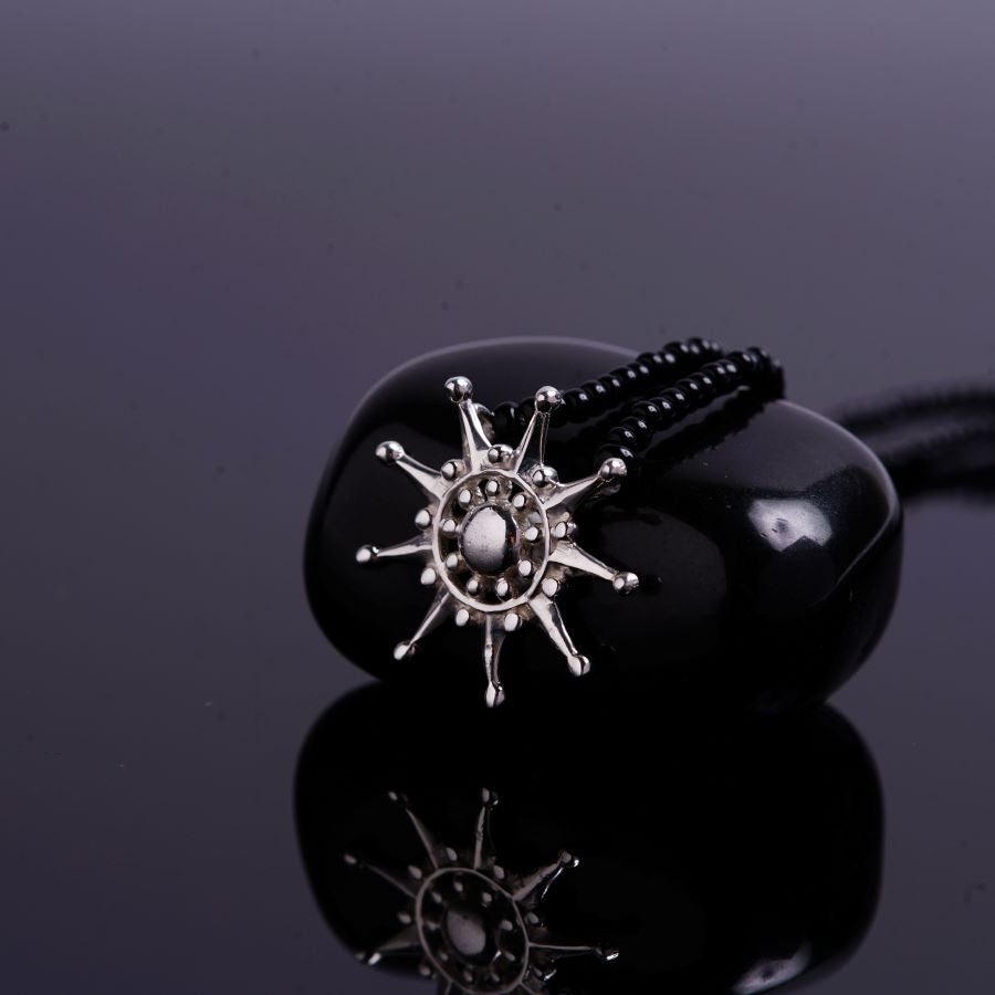 a black beaded necklace with a silver sun charm
