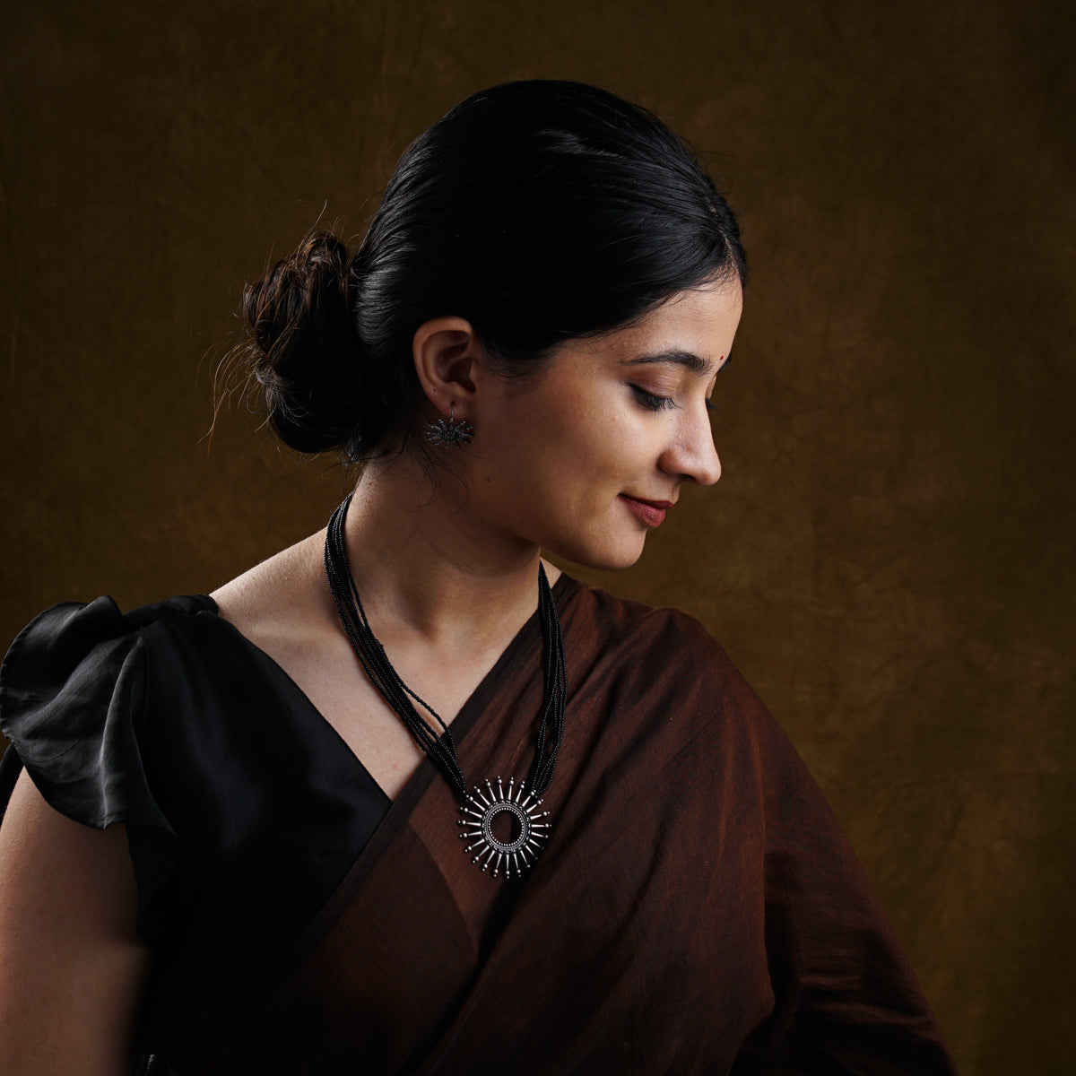 a woman wearing a necklace and a brown dress
