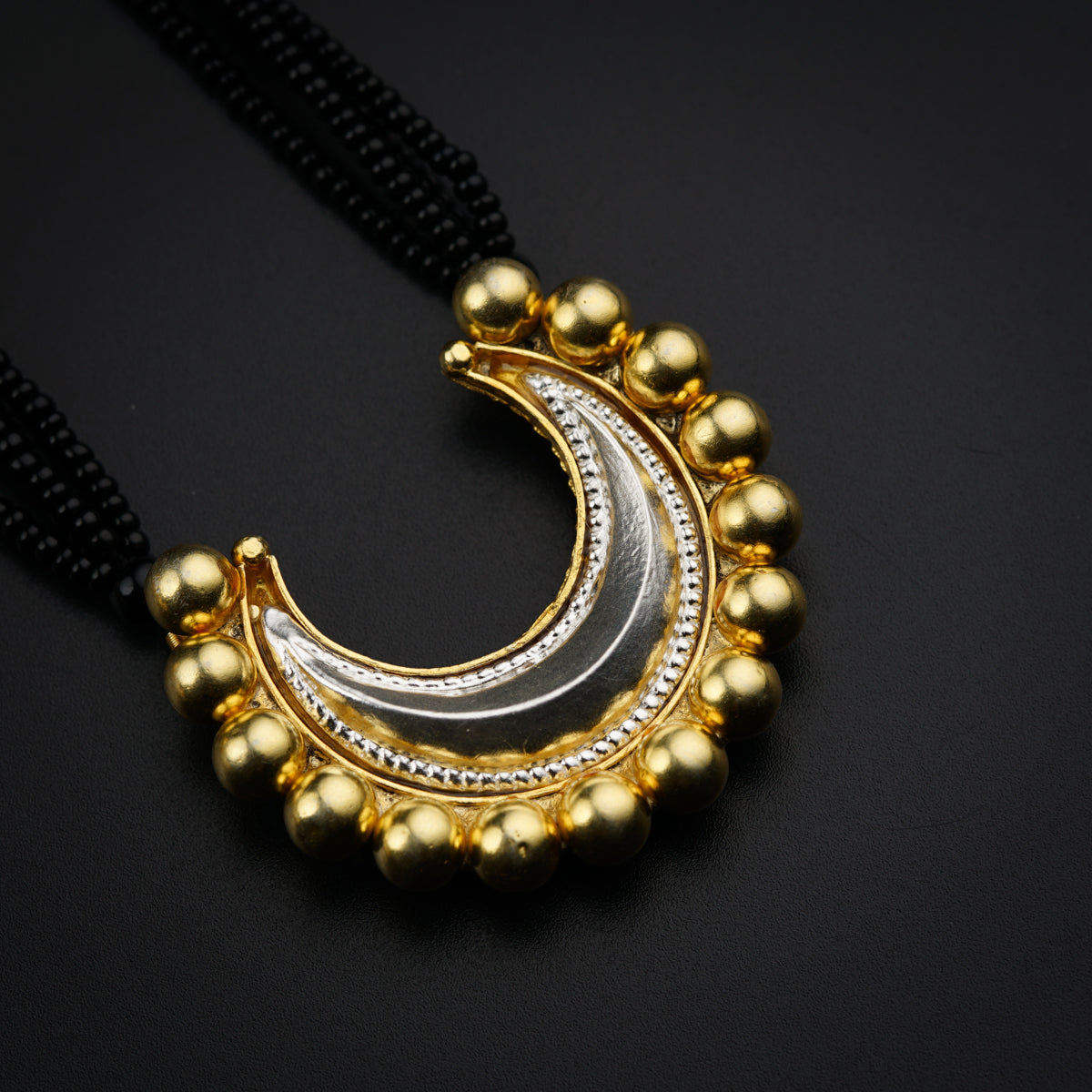 a gold and silver necklace with beads on a black background