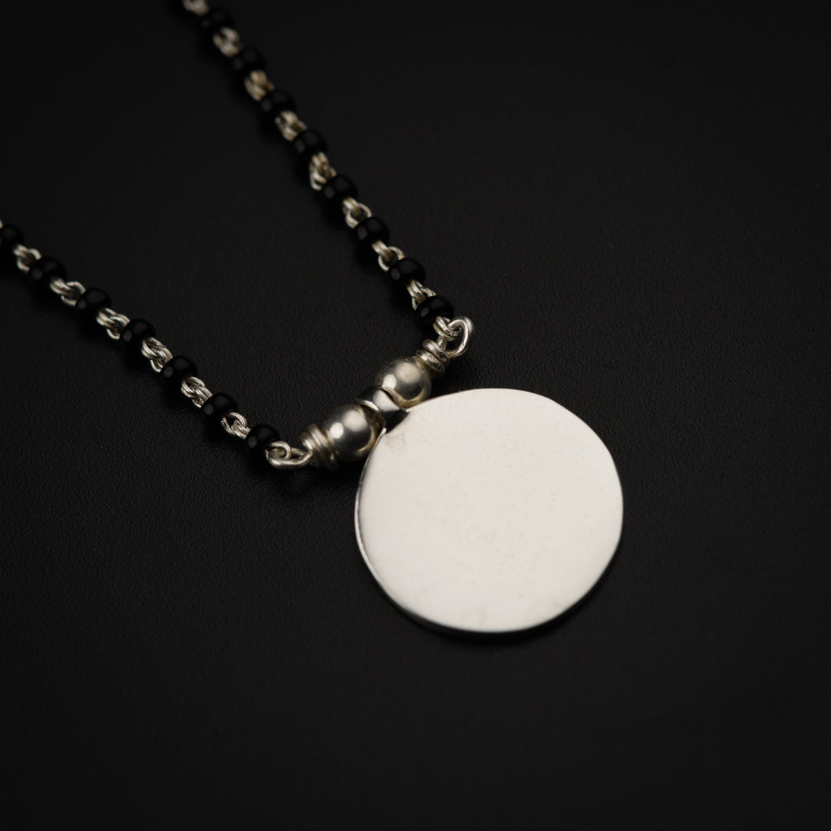 a silver disc on a chain on a black surface
