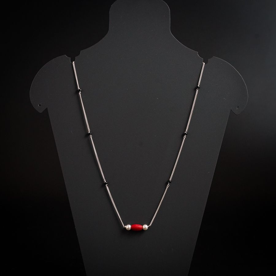 a necklace on a mannequin with a red bead