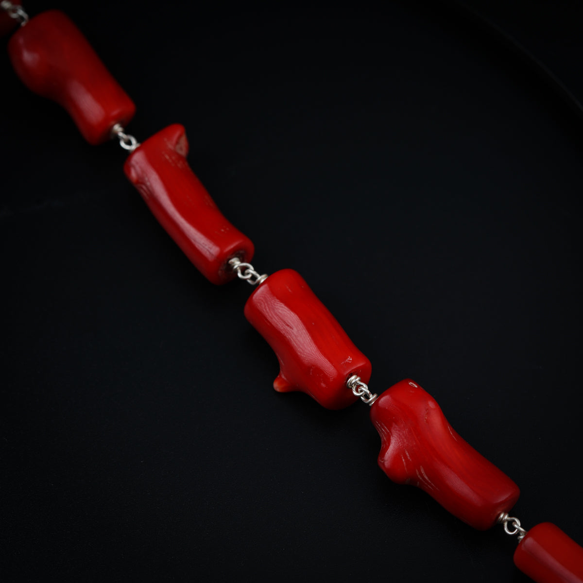 a red necklace with a silver chain on a black surface