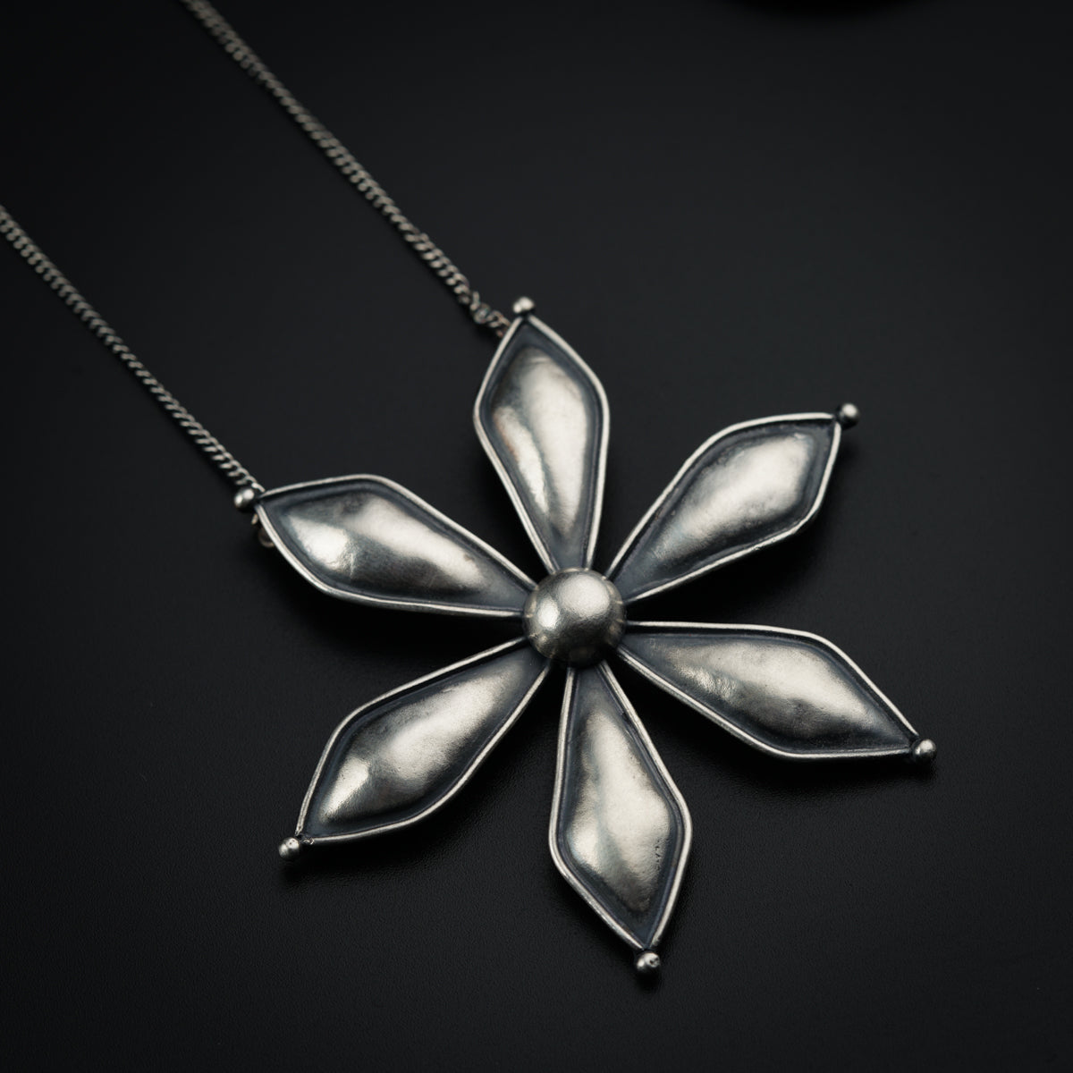 a silver flower necklace on a black surface