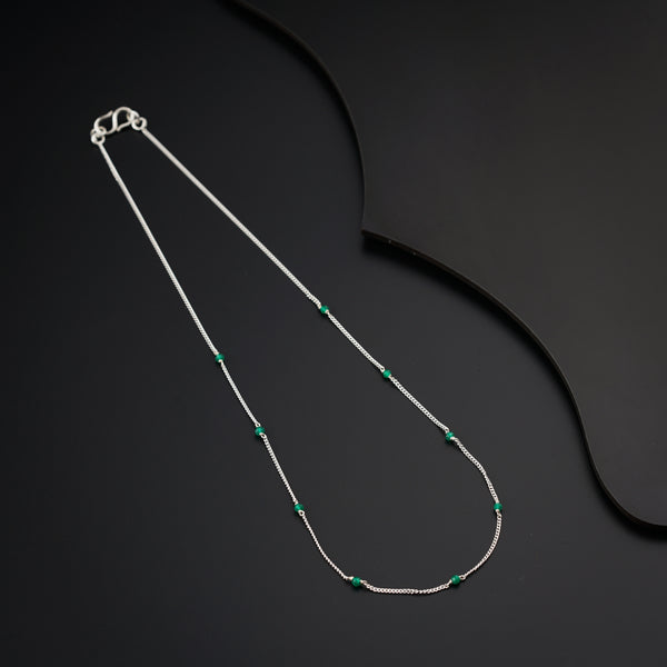a silver necklace with a green bead on a black background