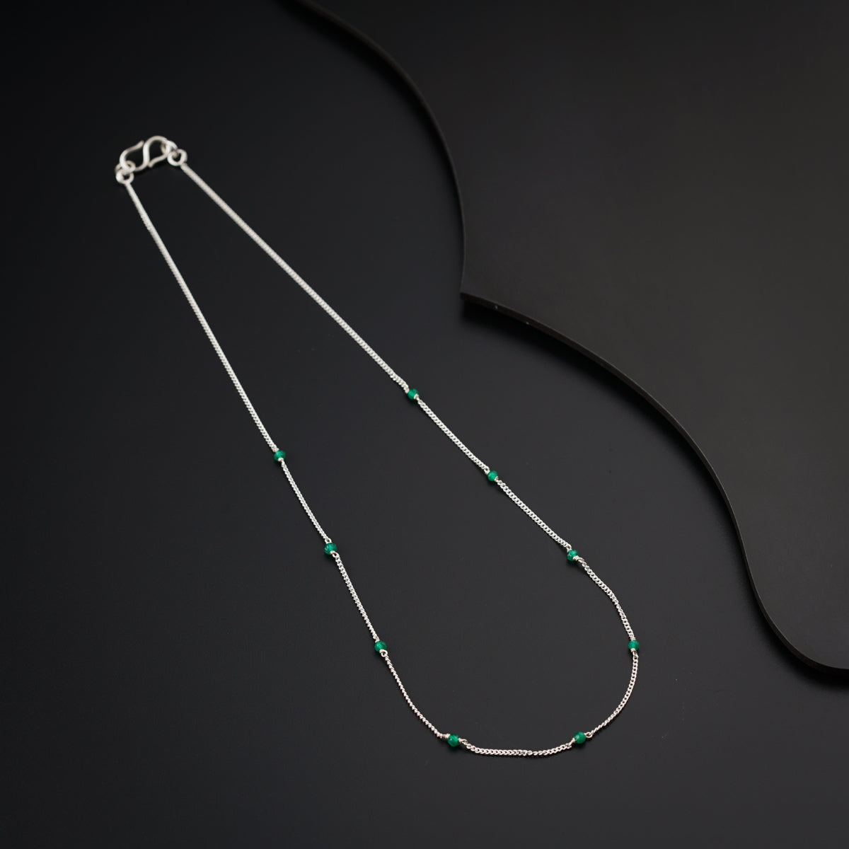 a silver necklace with a green bead on a black background