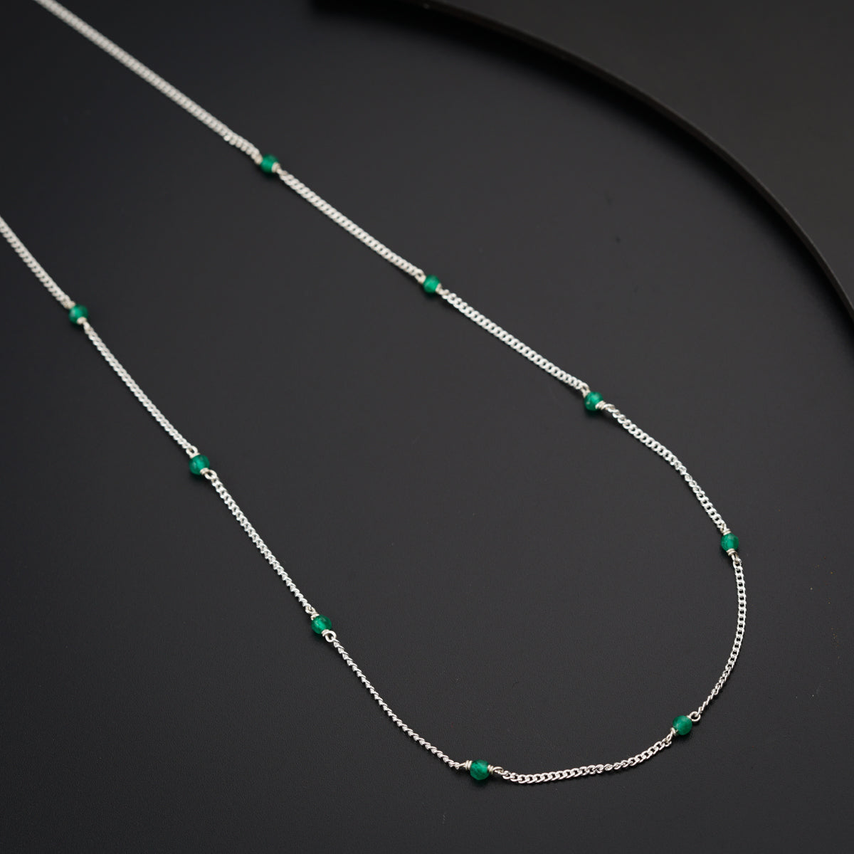 a silver necklace with green beads on a black surface