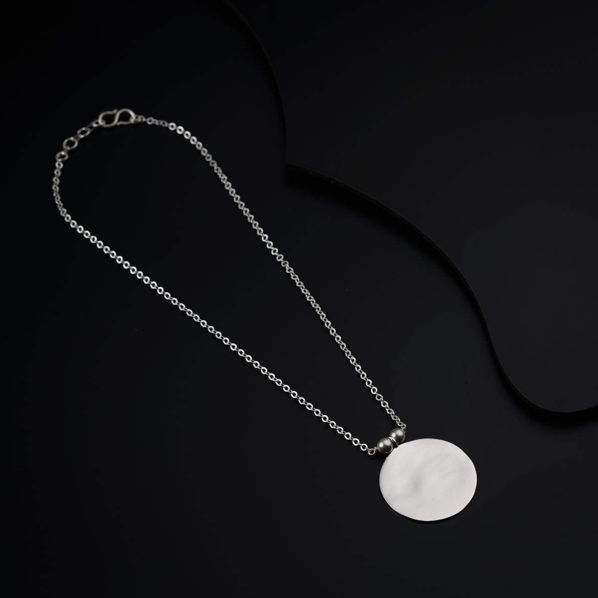 a white disc on a silver chain on a black background