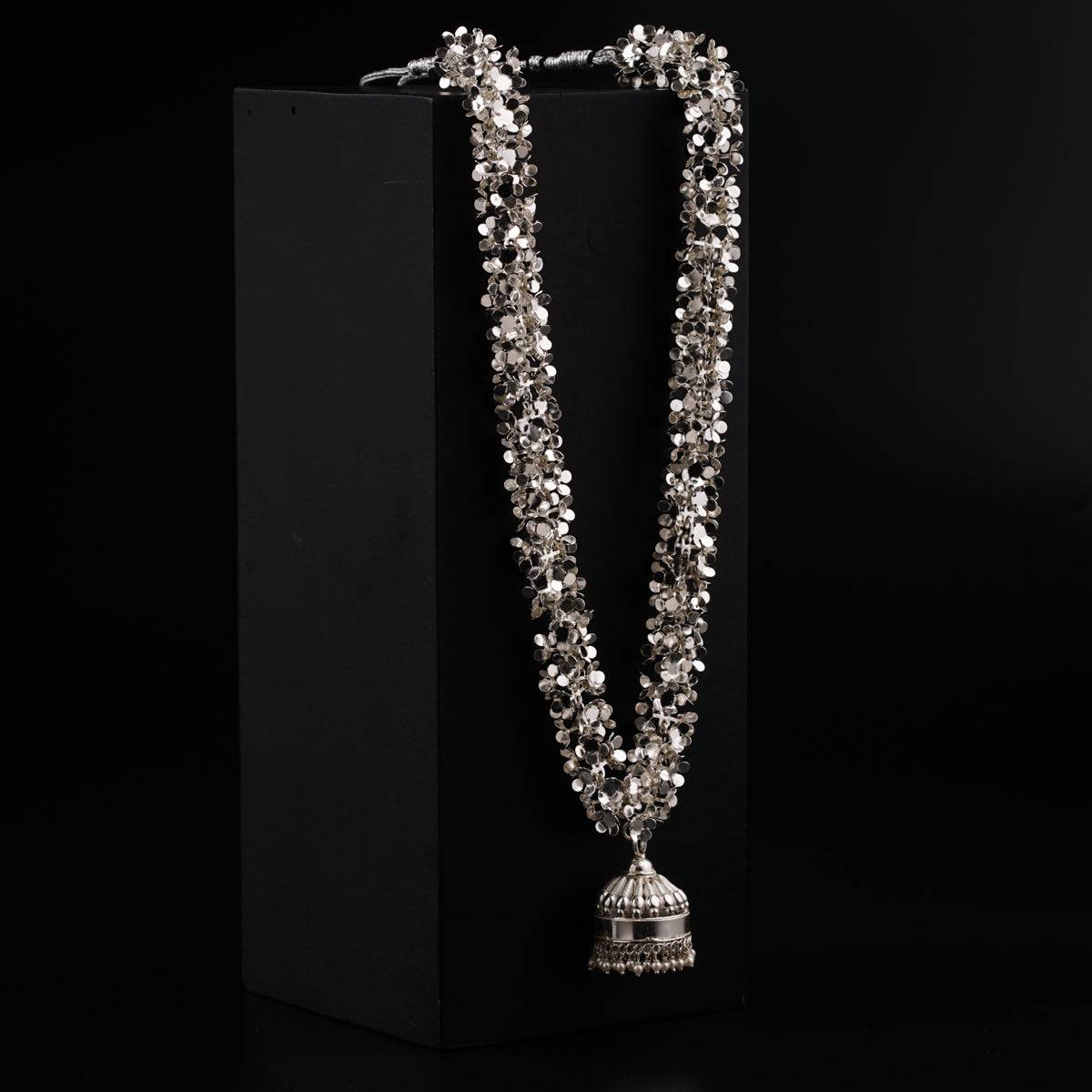 a silver necklace with a bell on a black background