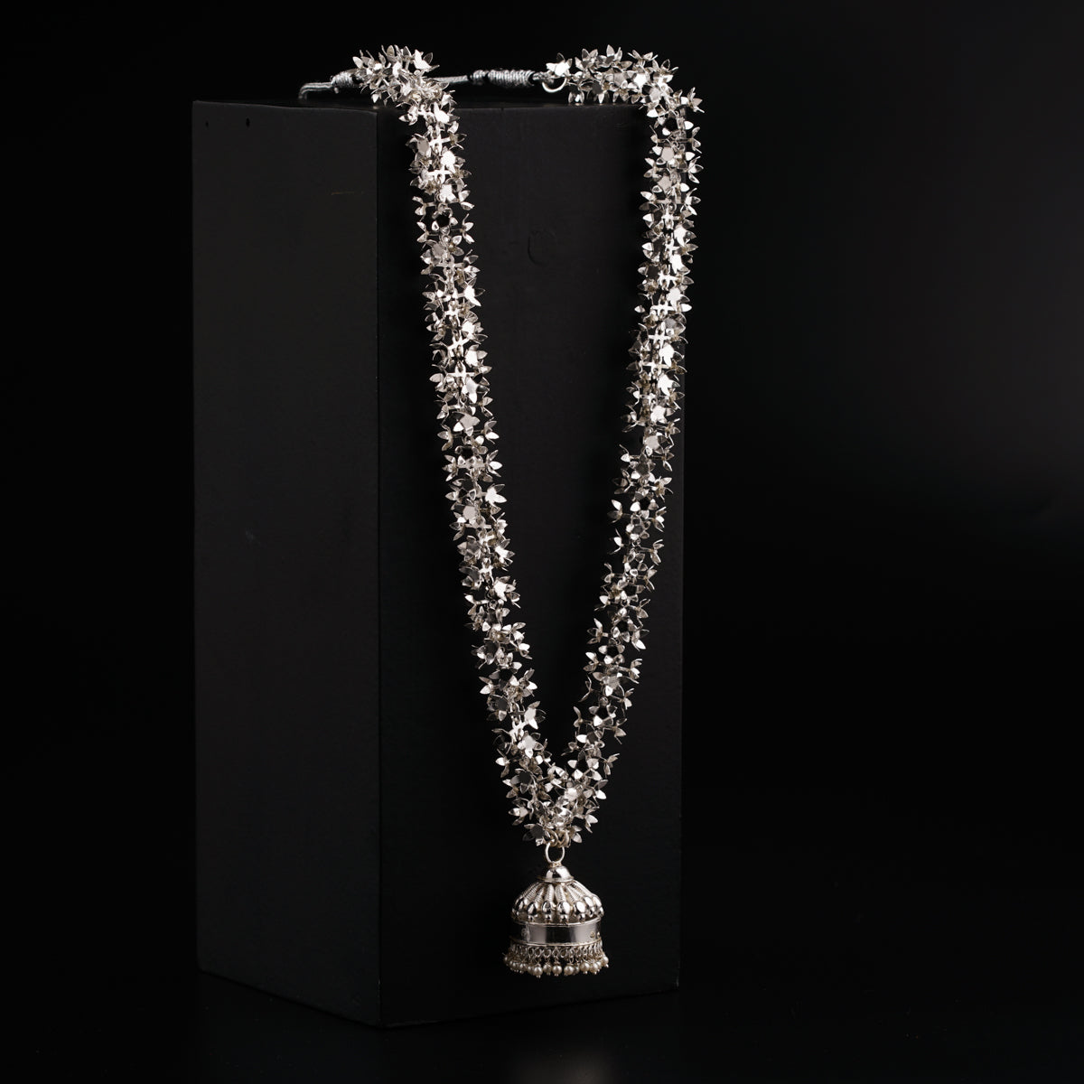 a silver necklace with a bell on a black background