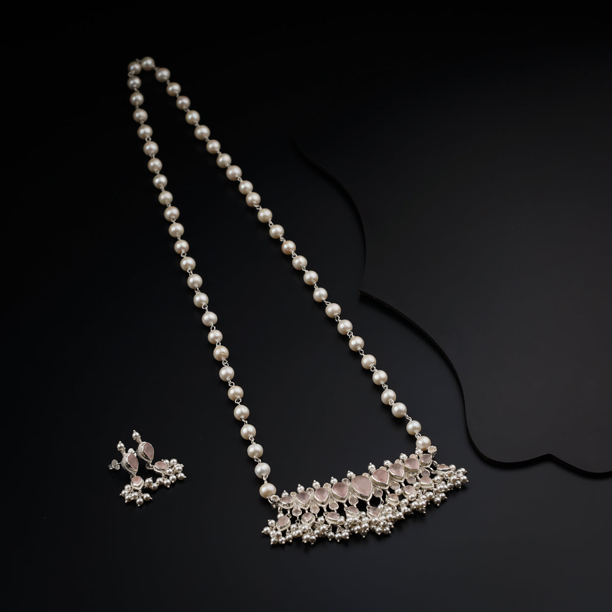 a necklace and earring with pearls on a black surface