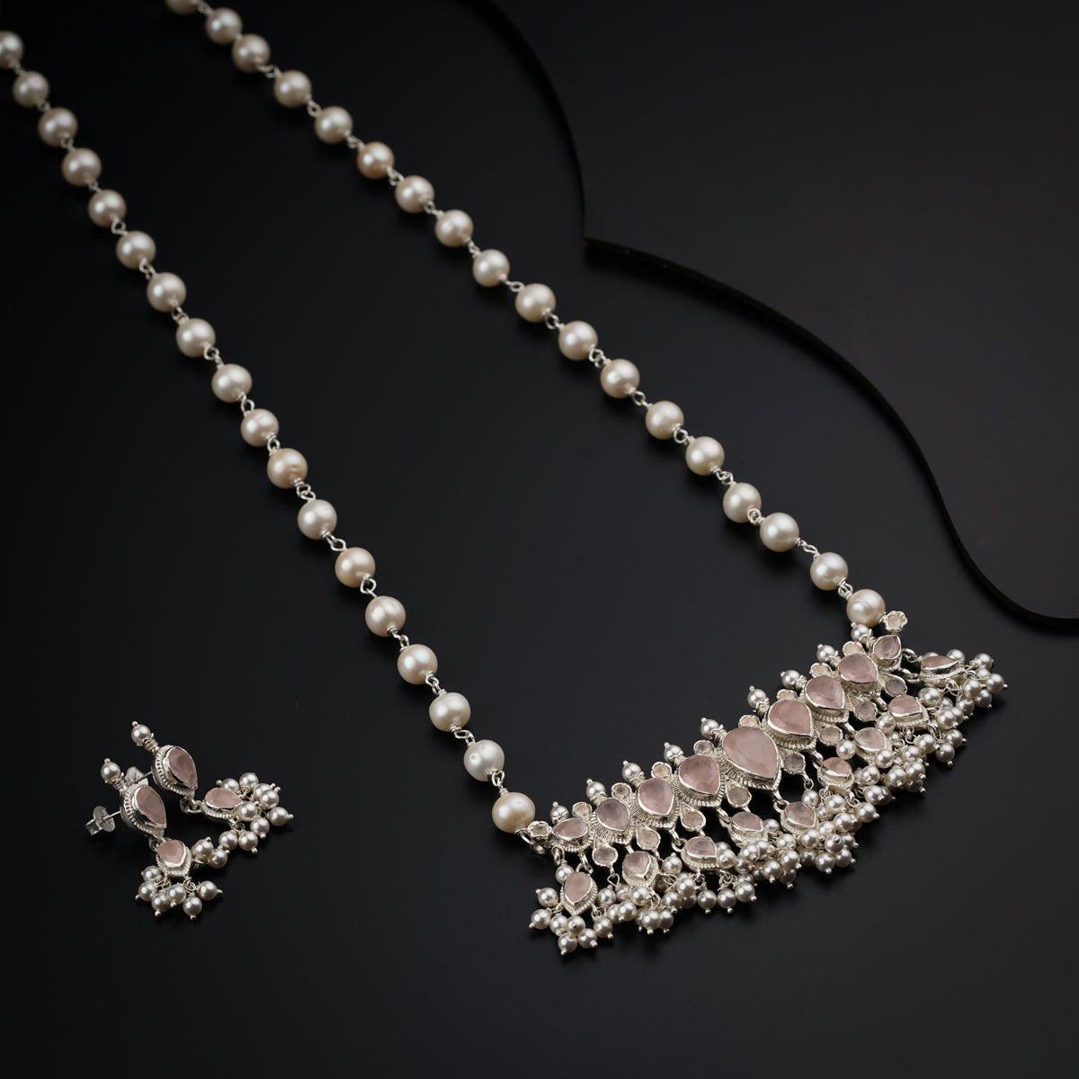 a necklace and earring with pearls on a black surface