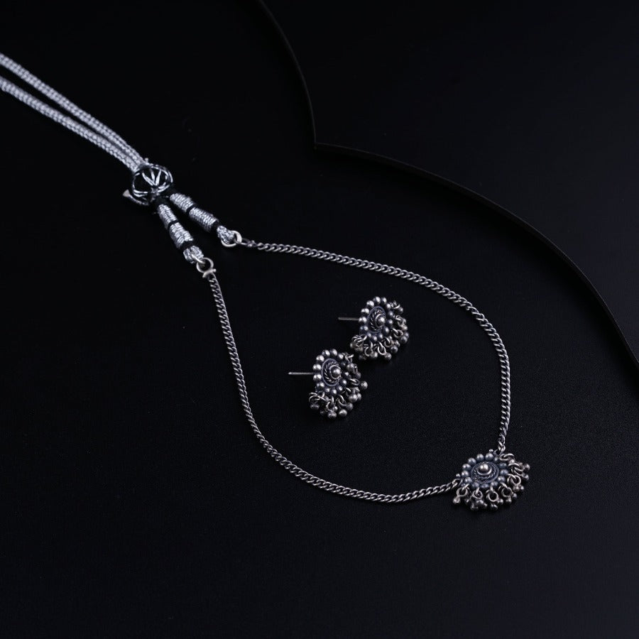 a silver necklace and earring set on a black surface