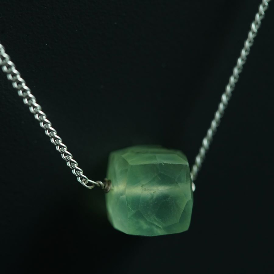 a green necklace with a silver chain on a black background