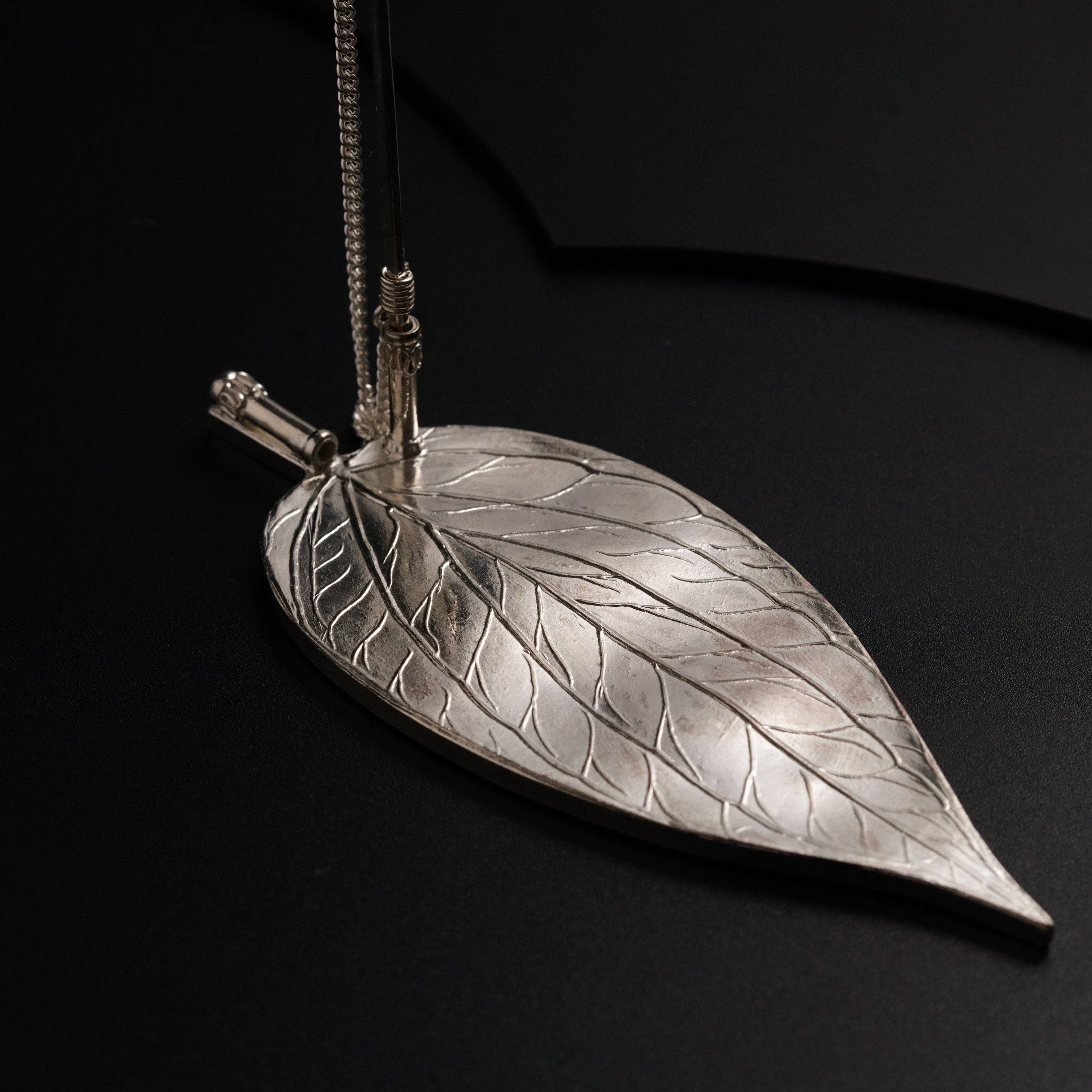 a silver leaf pendant on a black surface