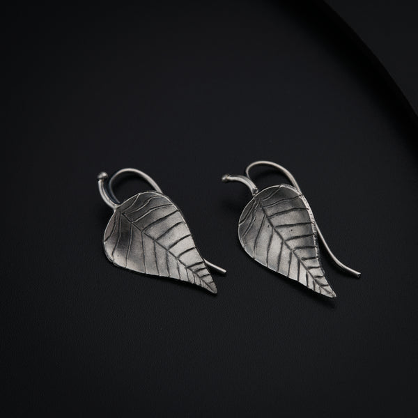 a pair of silver leaf earrings on a black surface
