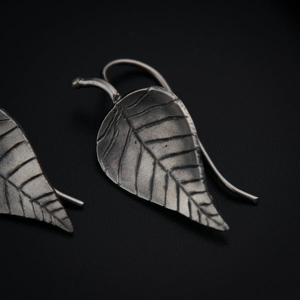 a pair of silver leaf earrings on a black surface