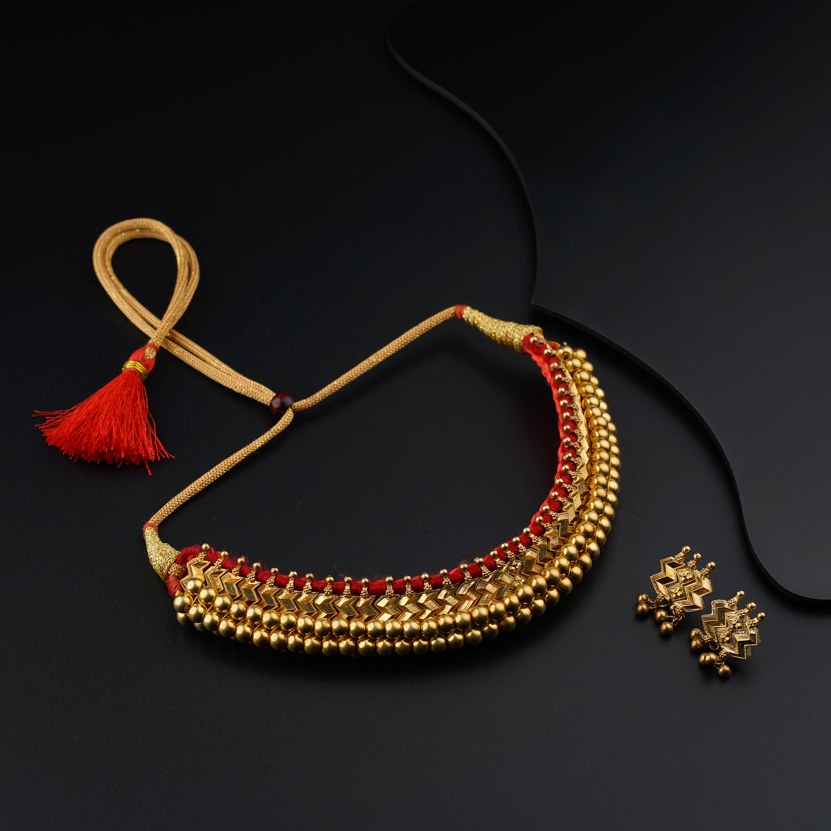 a gold necklace with red beads and a red tassel