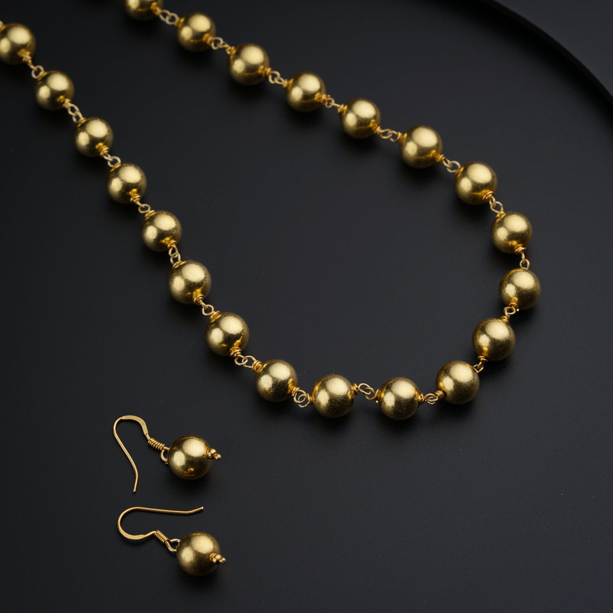 a gold bead necklace and earring set on a black surface