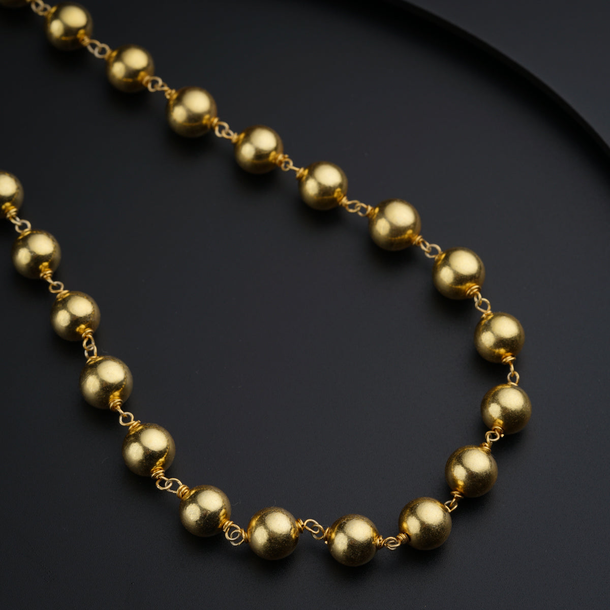 a gold beaded necklace on a black surface