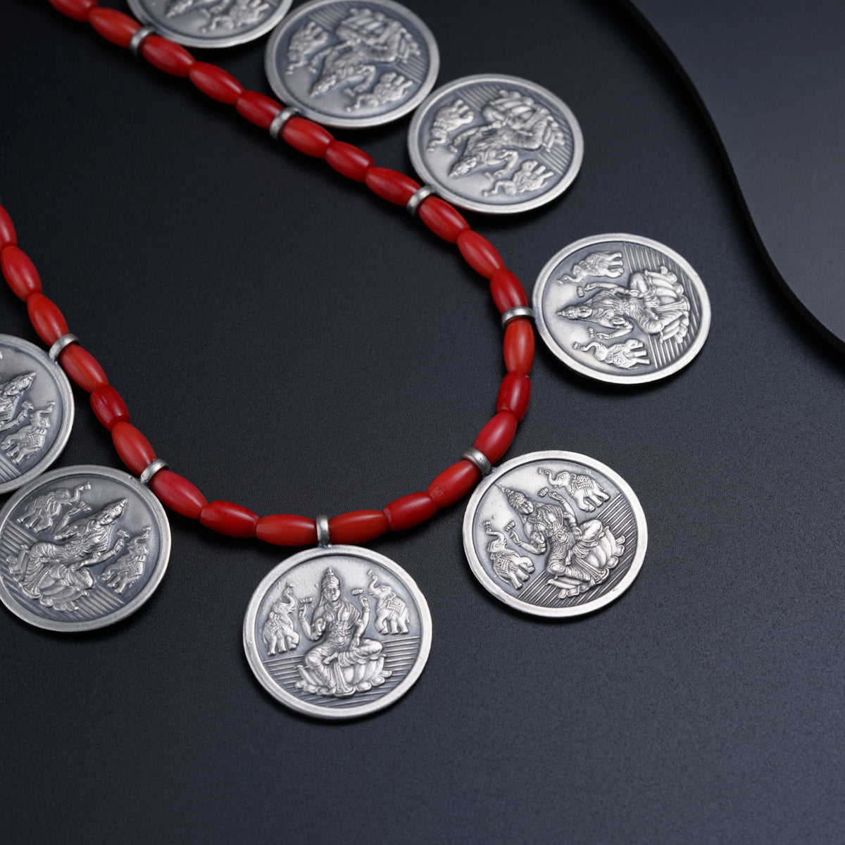 a red necklace with silver coins on a black surface