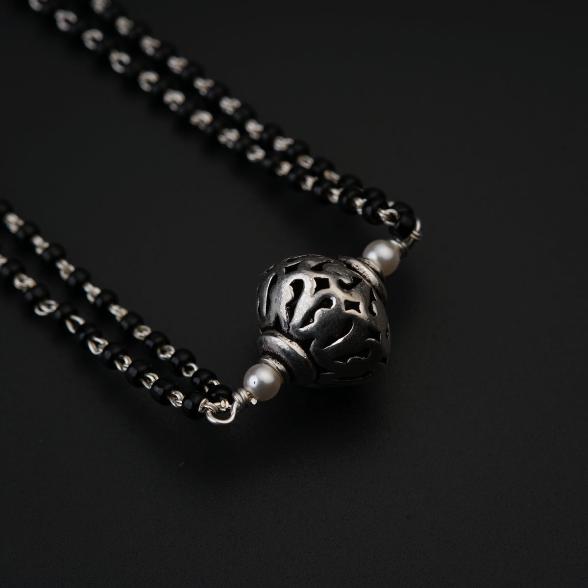 a black bead necklace with a silver ball on a black background