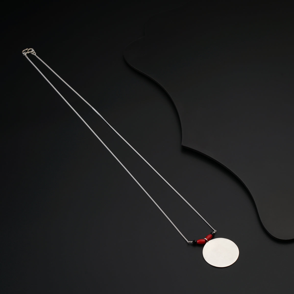 a necklace with a white disc and a red bea