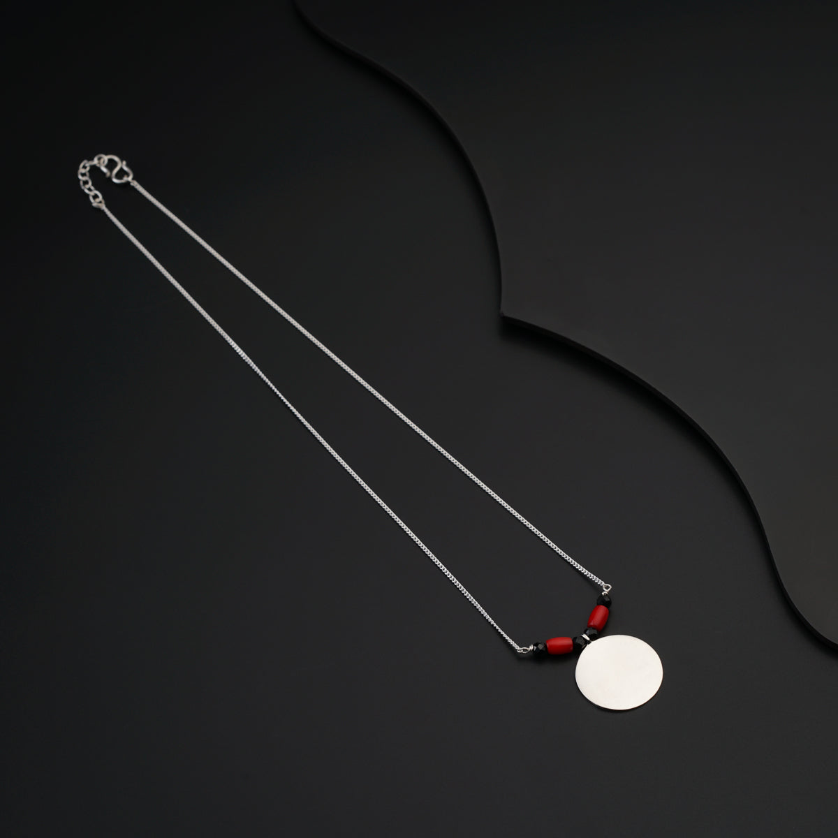 a necklace with a white disc and a red bead