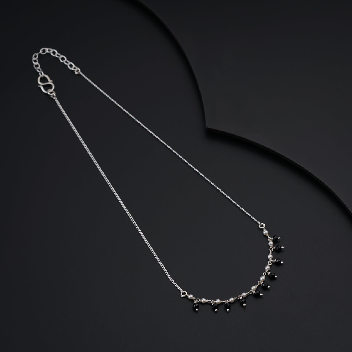 a silver necklace with black beads on a black background