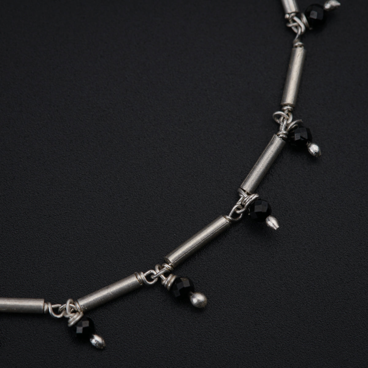 a silver necklace with black beads on a black surface
