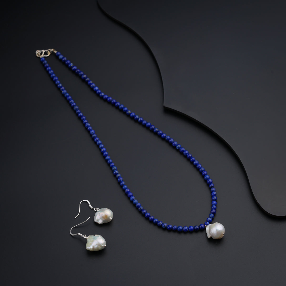 a necklace and earring set with pearls on a black background