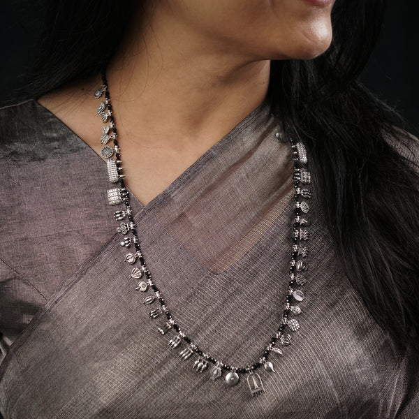 A person wearing a oxidized silver necklace with black spinel stones, with the necklace hanging around the neck and chest area.