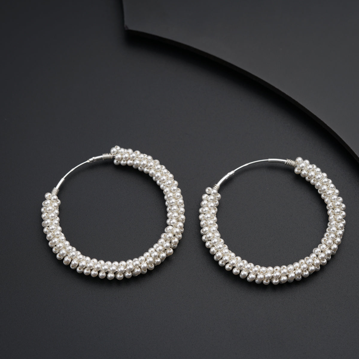 a pair of pearl hoop earrings on a black surface