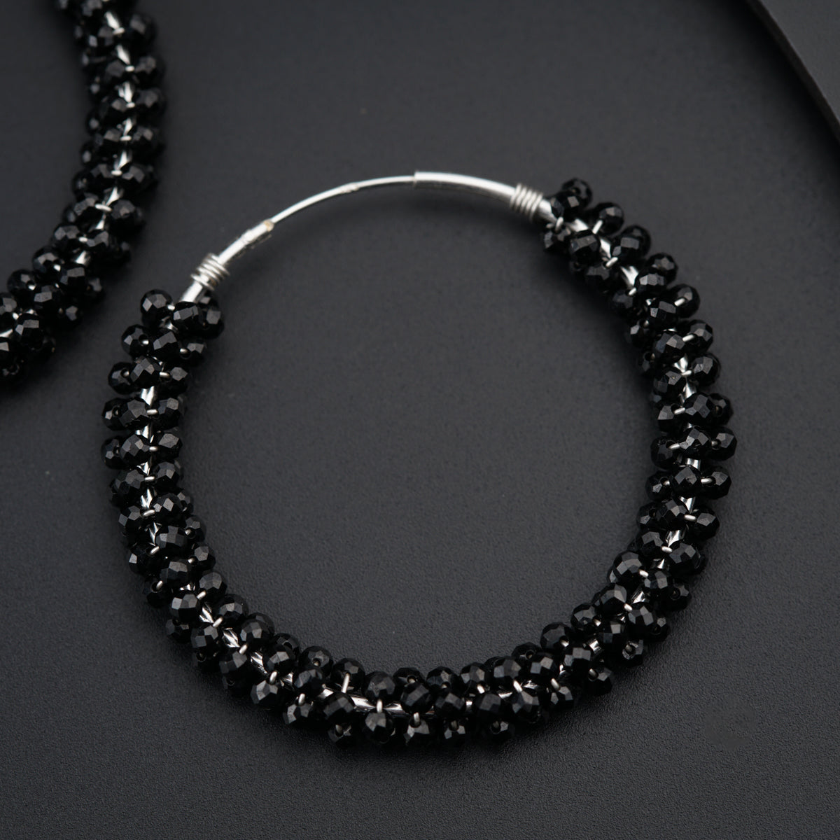 a pair of black beaded hoop earrings on a black surface