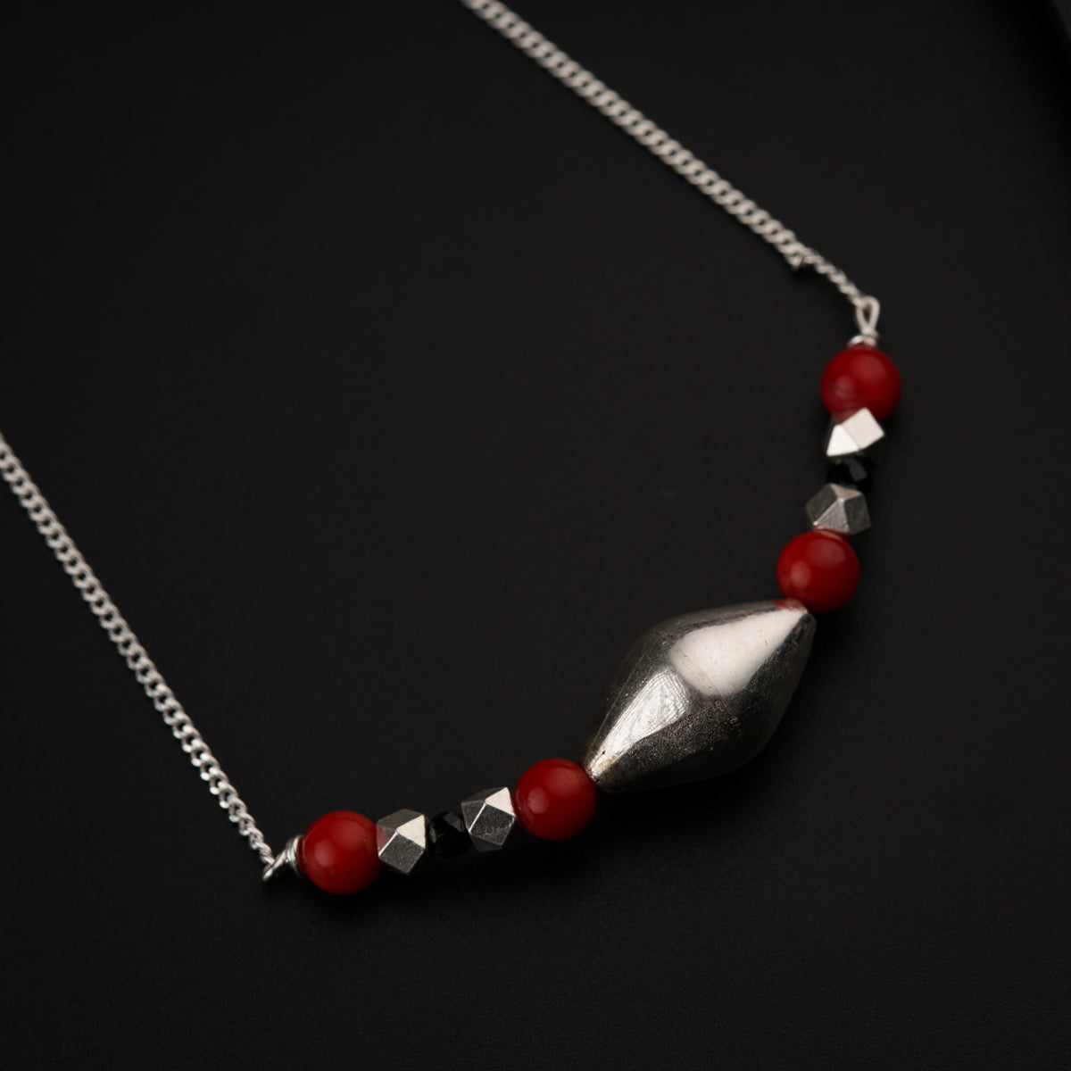 a silver necklace with red beads on a black surface