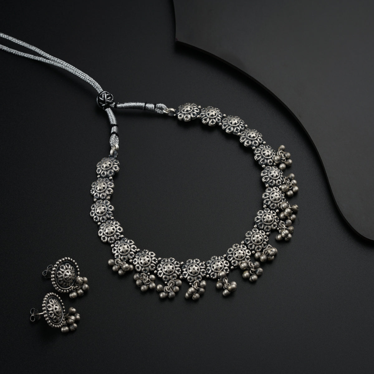a silver necklace and matching earrings on a black surface