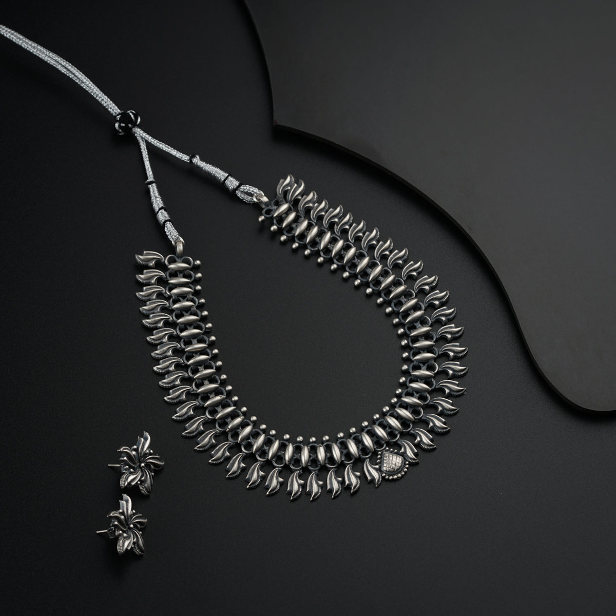 a silver necklace and earring on a black surface