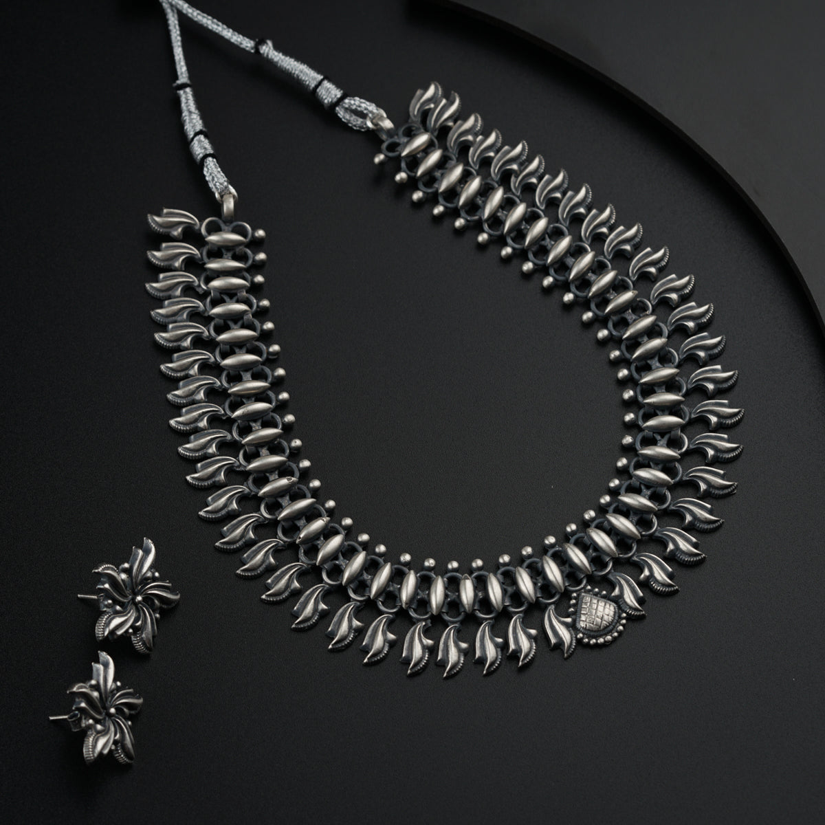 a silver necklace and earring on a black surface