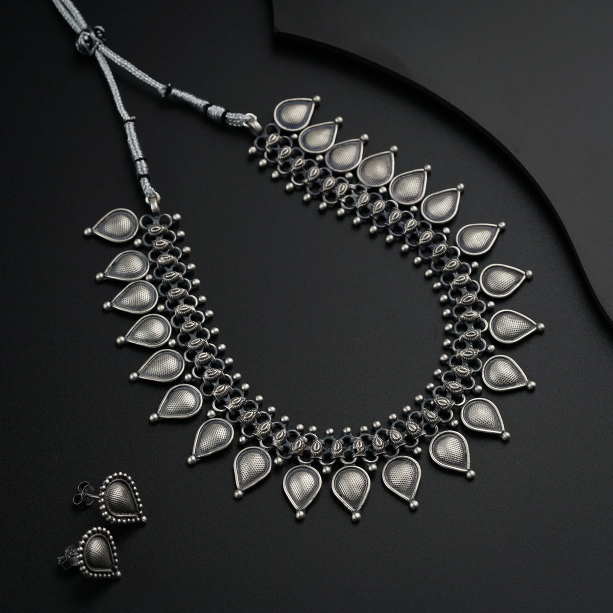 a silver necklace and matching earrings on a black surface