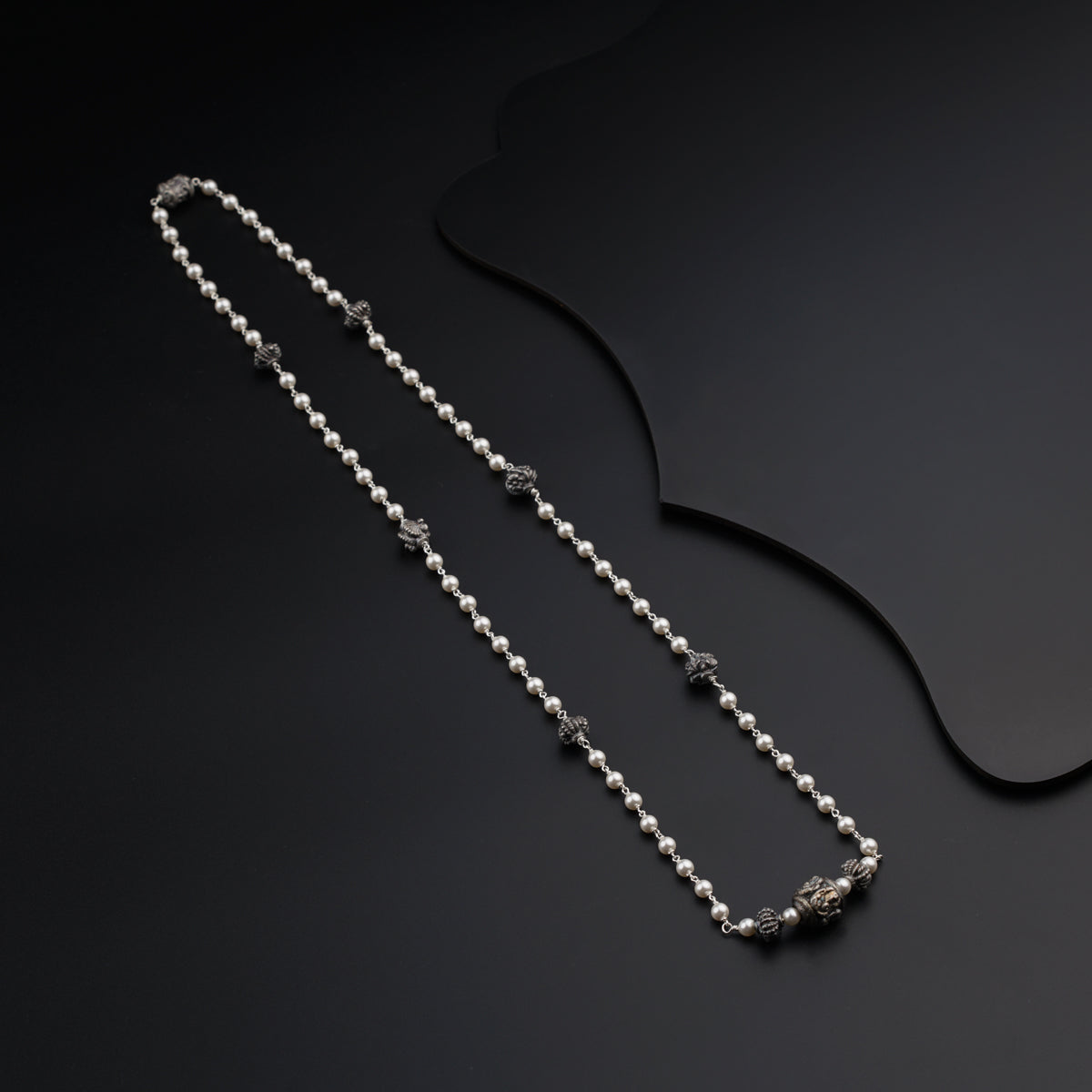 a silver chain with beads on a black surface