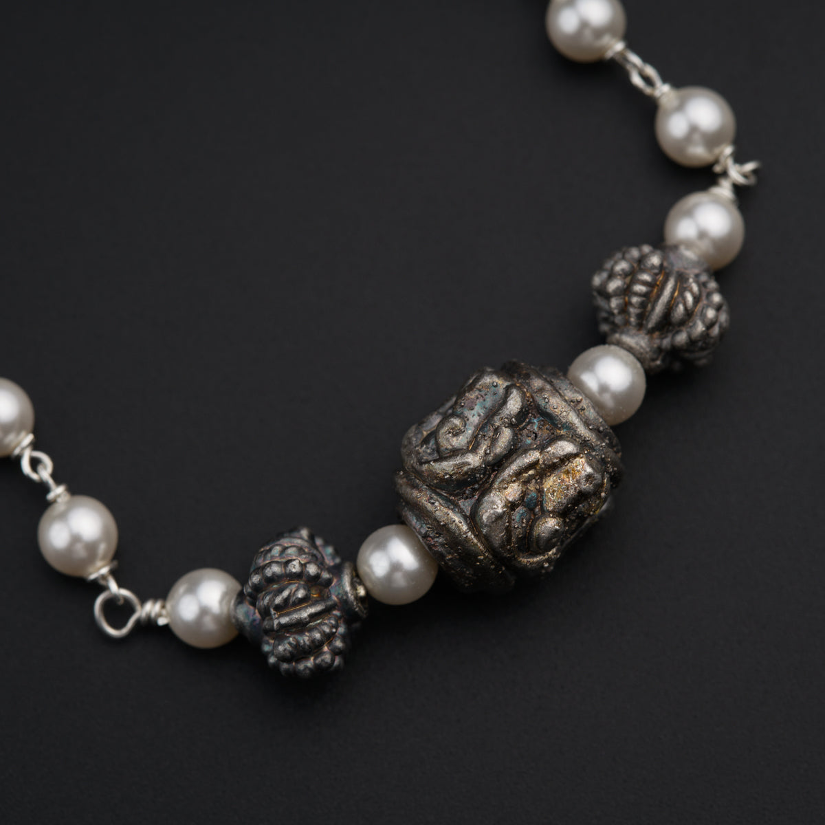 a silver bracelet with pearls and beads on a black surface