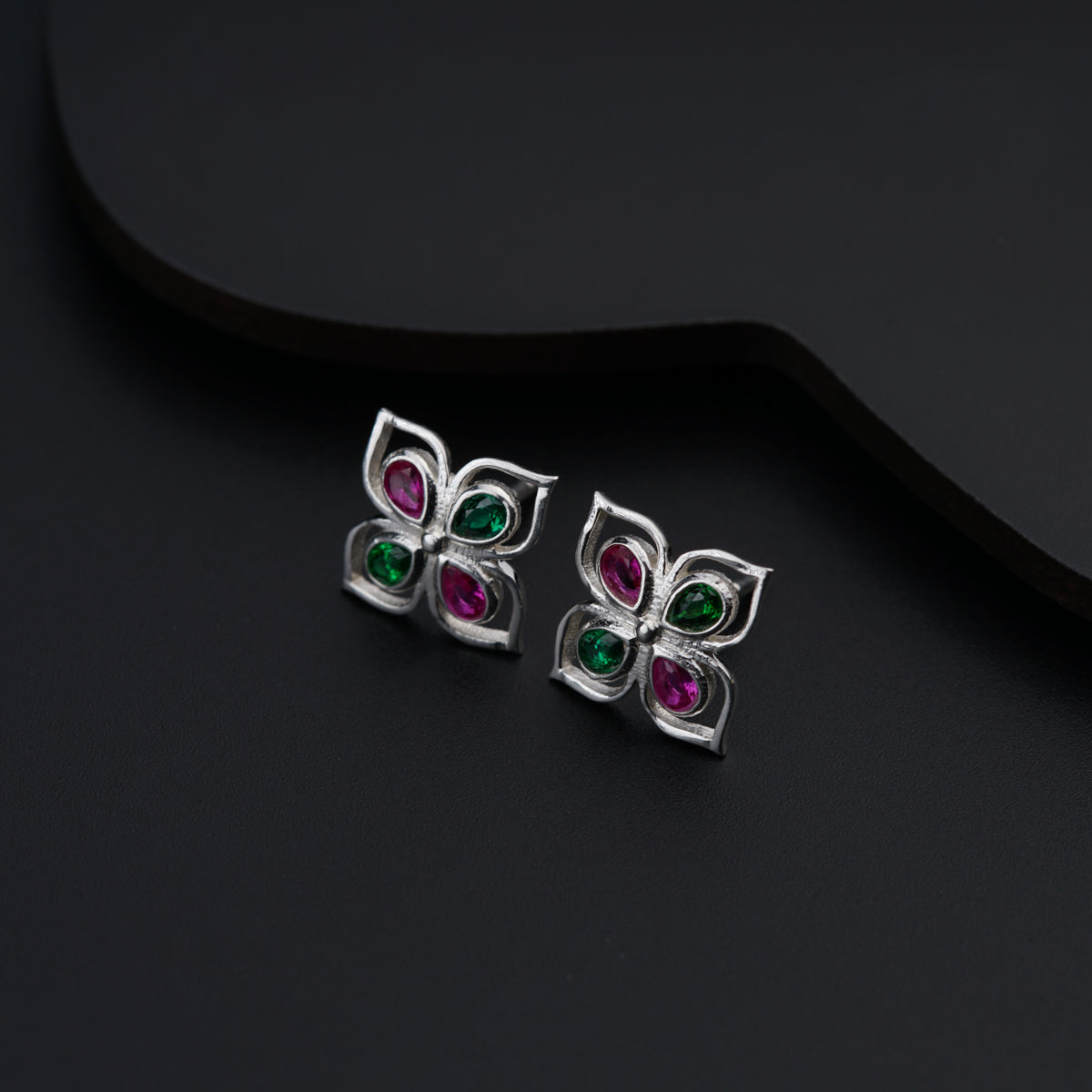 a pair of earrings with colorful stones on a black surface