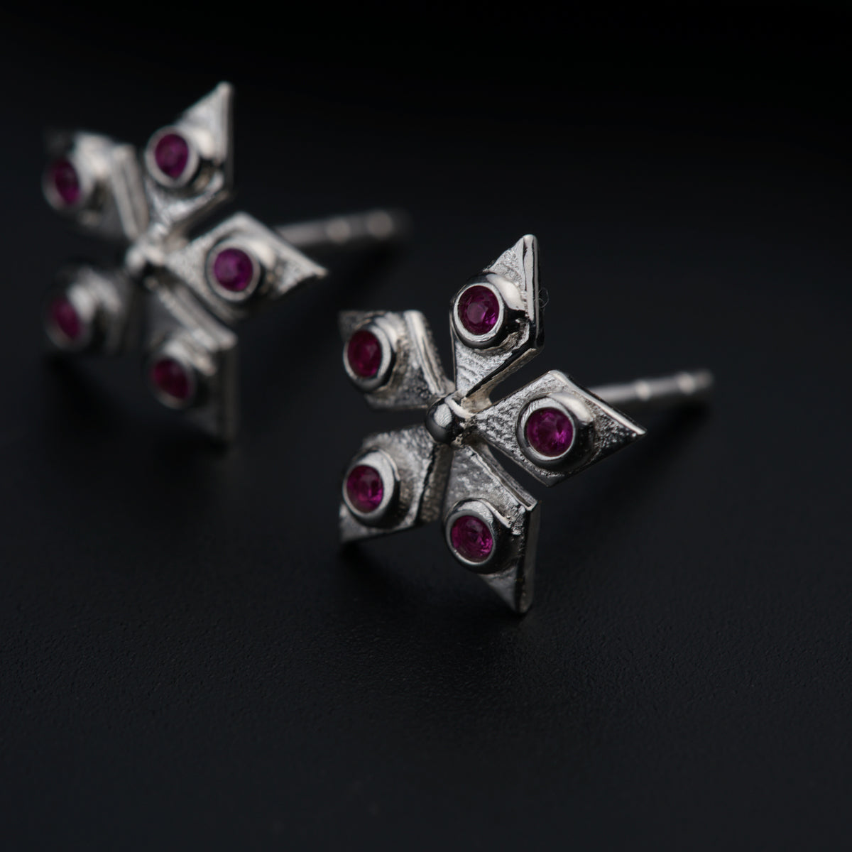 a pair of silver and ruby earrings on a black surface