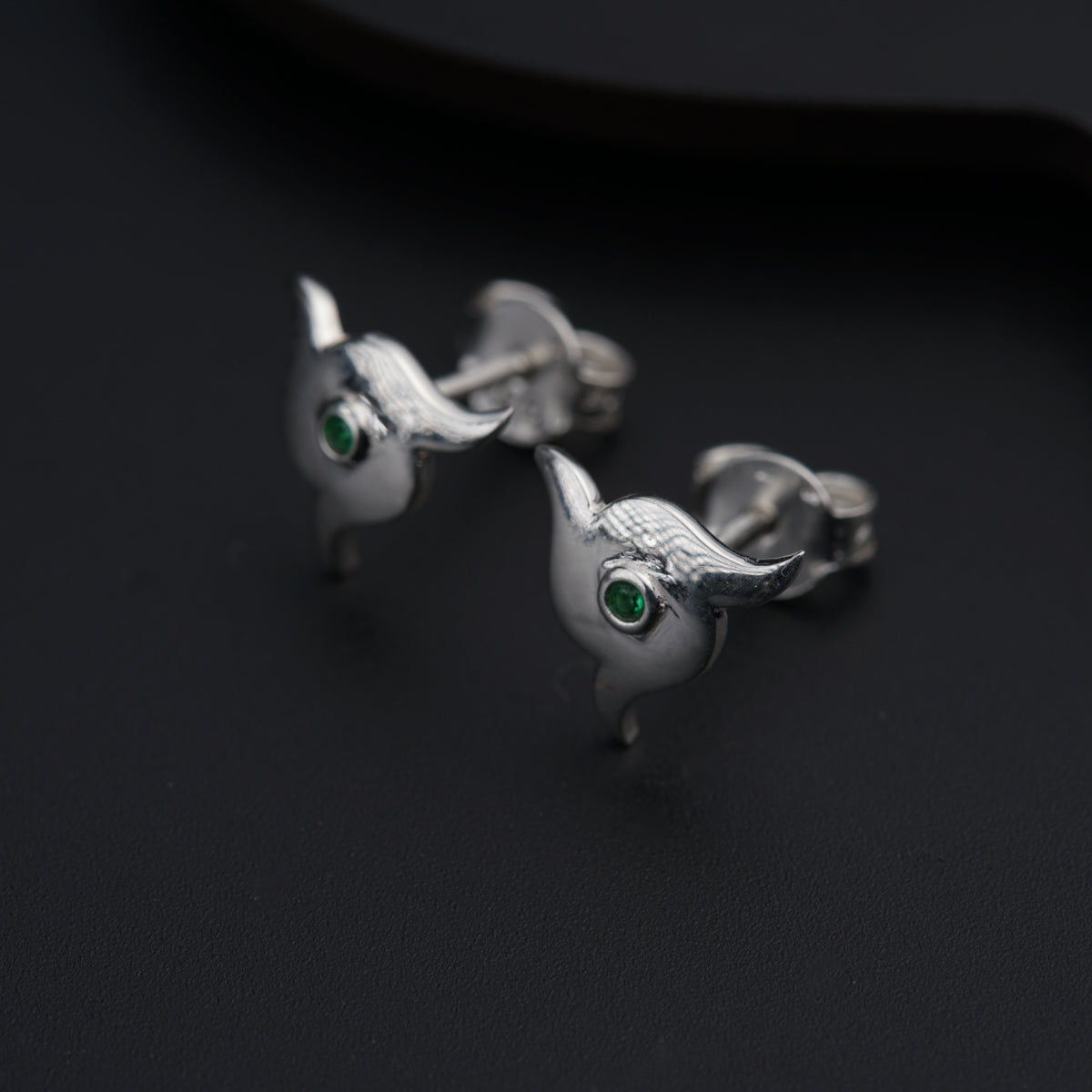 a pair of silver bird earrings with green eyes