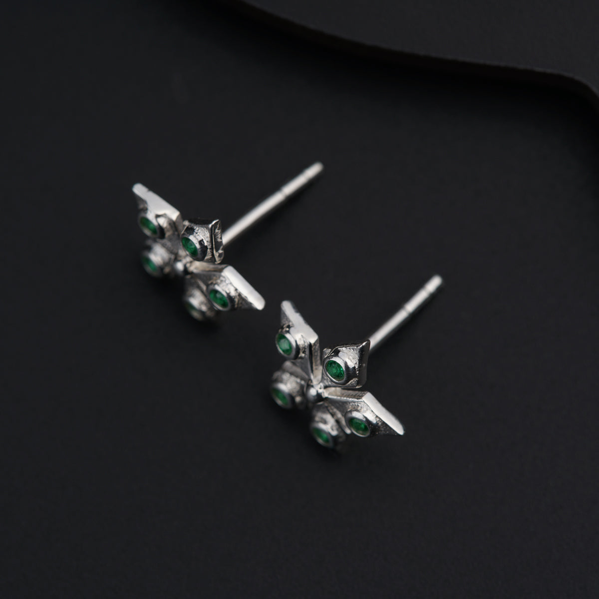 a pair of silver and green earrings on a black surface