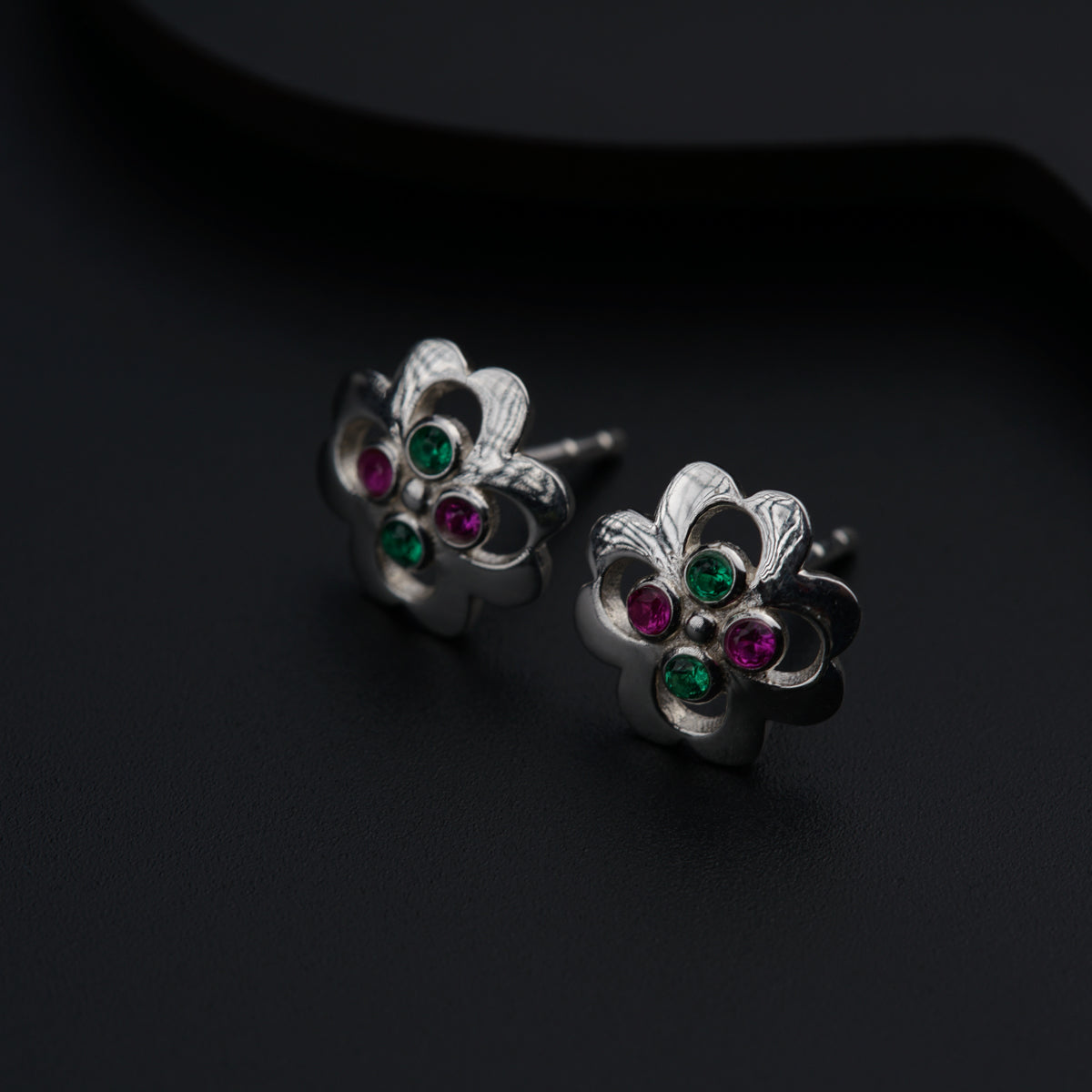 a pair of silver earrings with green and red stones