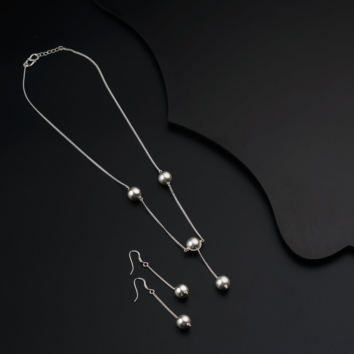 a pair of silver necklaces and earrings on a black background
