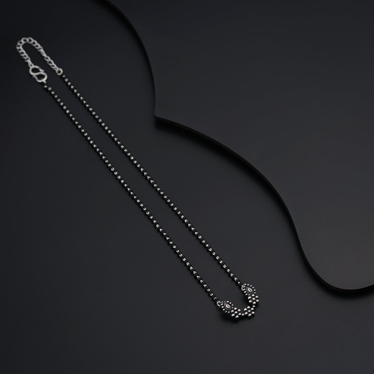 a black necklace with a white diamond on a black background
