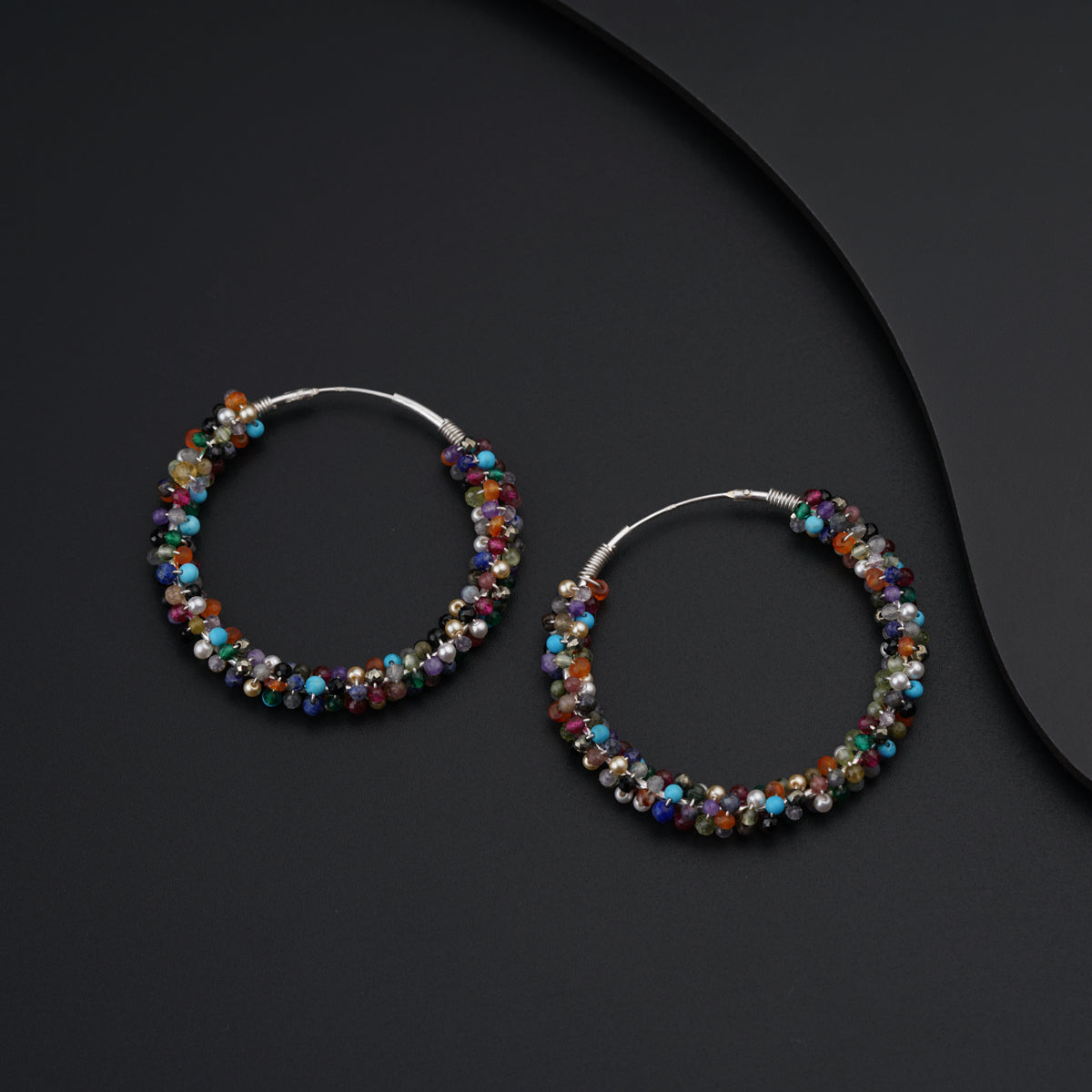 a pair of beaded hoop earrings on a black surface