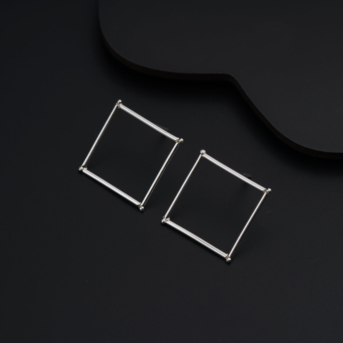a pair of square earrings sitting on top of a black surface